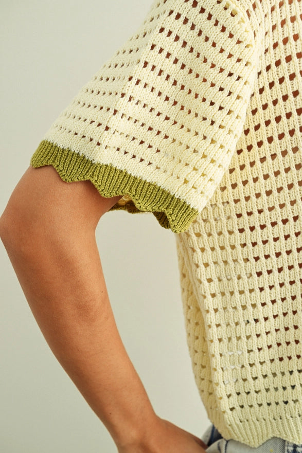Close-up of a person wearing a textured beige sweater with green trim on a neutral background