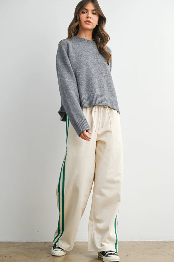 Woman wearing a gray sweater and cream pants with green stripes against a white background