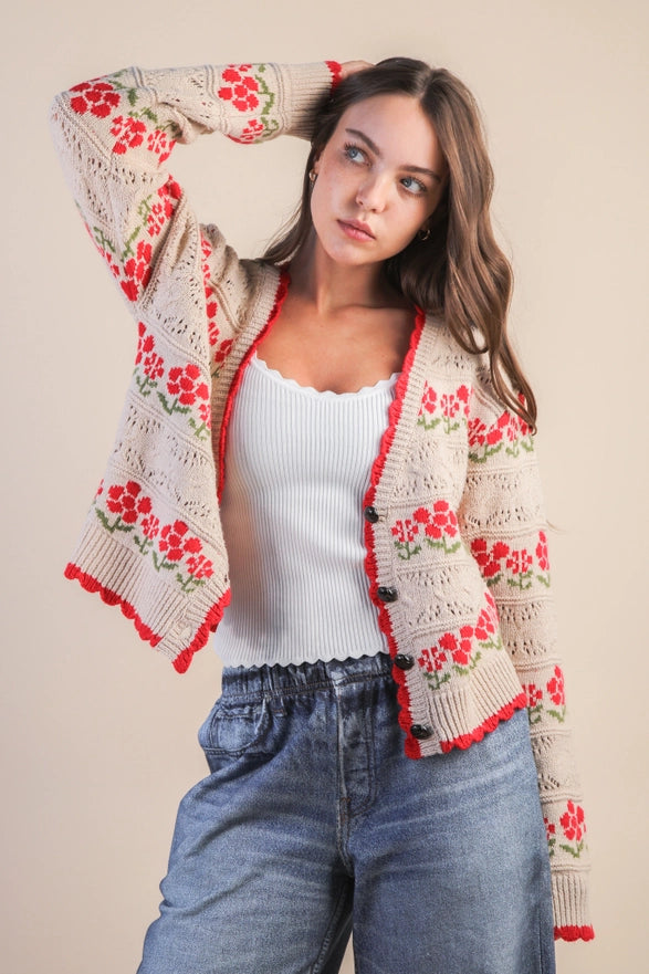 Woman wearing a floral crochet cardigan over a white top and blue jeans on a beige background