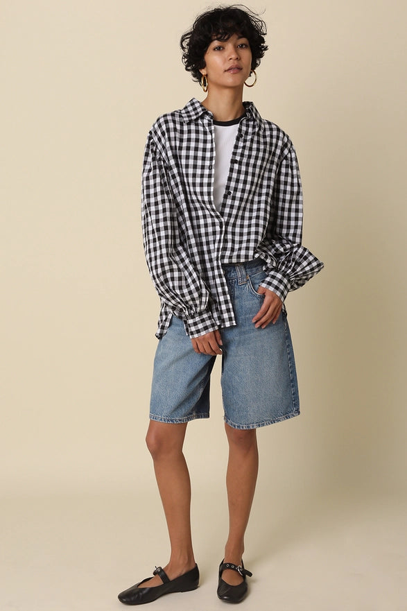 Person wearing a black and white checkered shirt with denim shorts on a beige background
