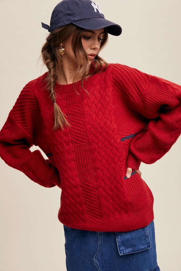Woman standing against a plain background wearing a Red pull over sweater