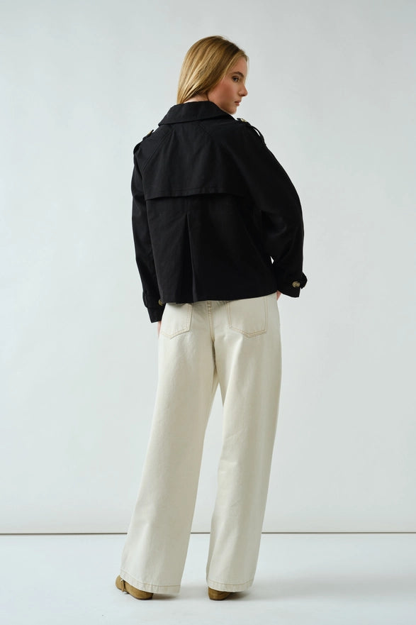 Person wearing a black jacket and white pants on a plain background