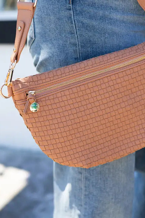 Brown woven handbag with gold accents held by a person wearing blue jeans.