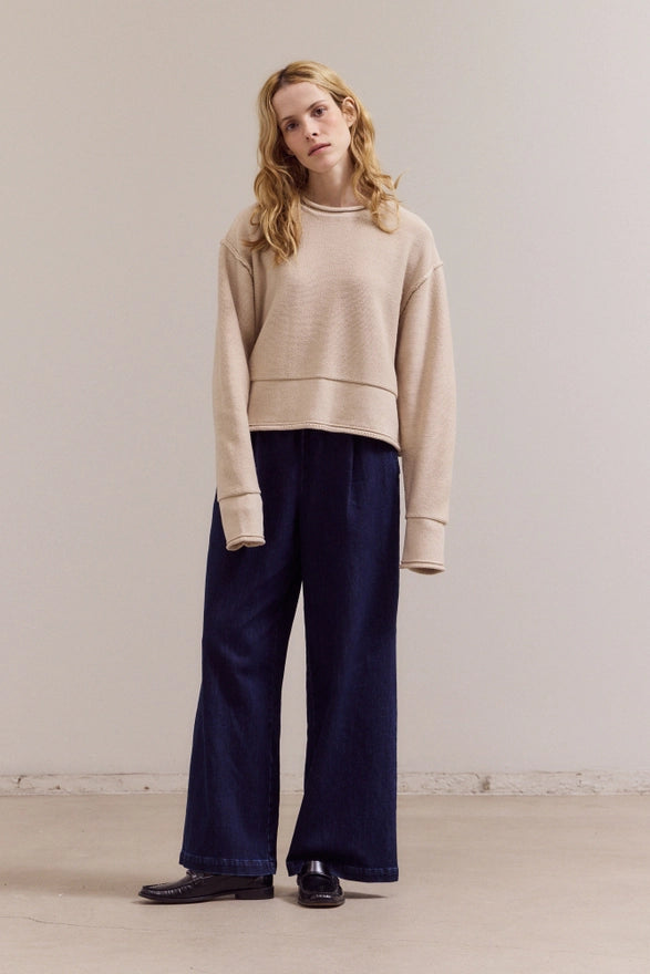 Woman wearing a beige sweater and navy pants against a plain background