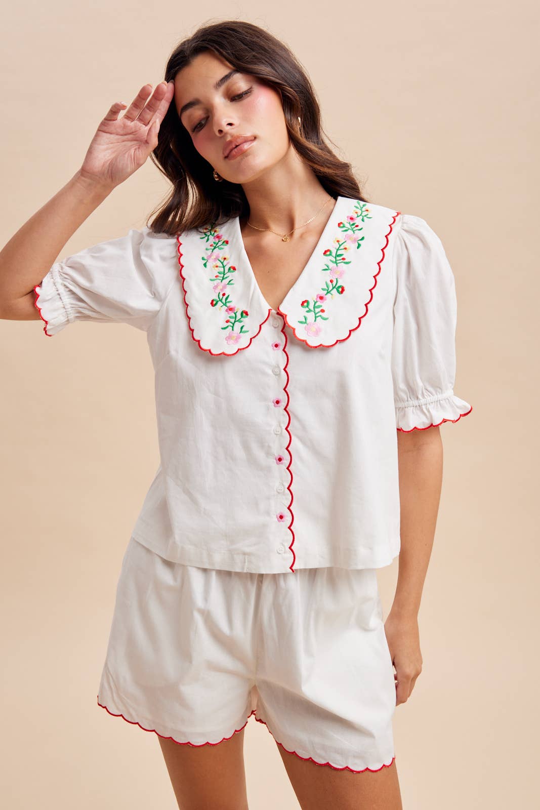 Woman wearing a white embroidered top and shorts set on a beige background