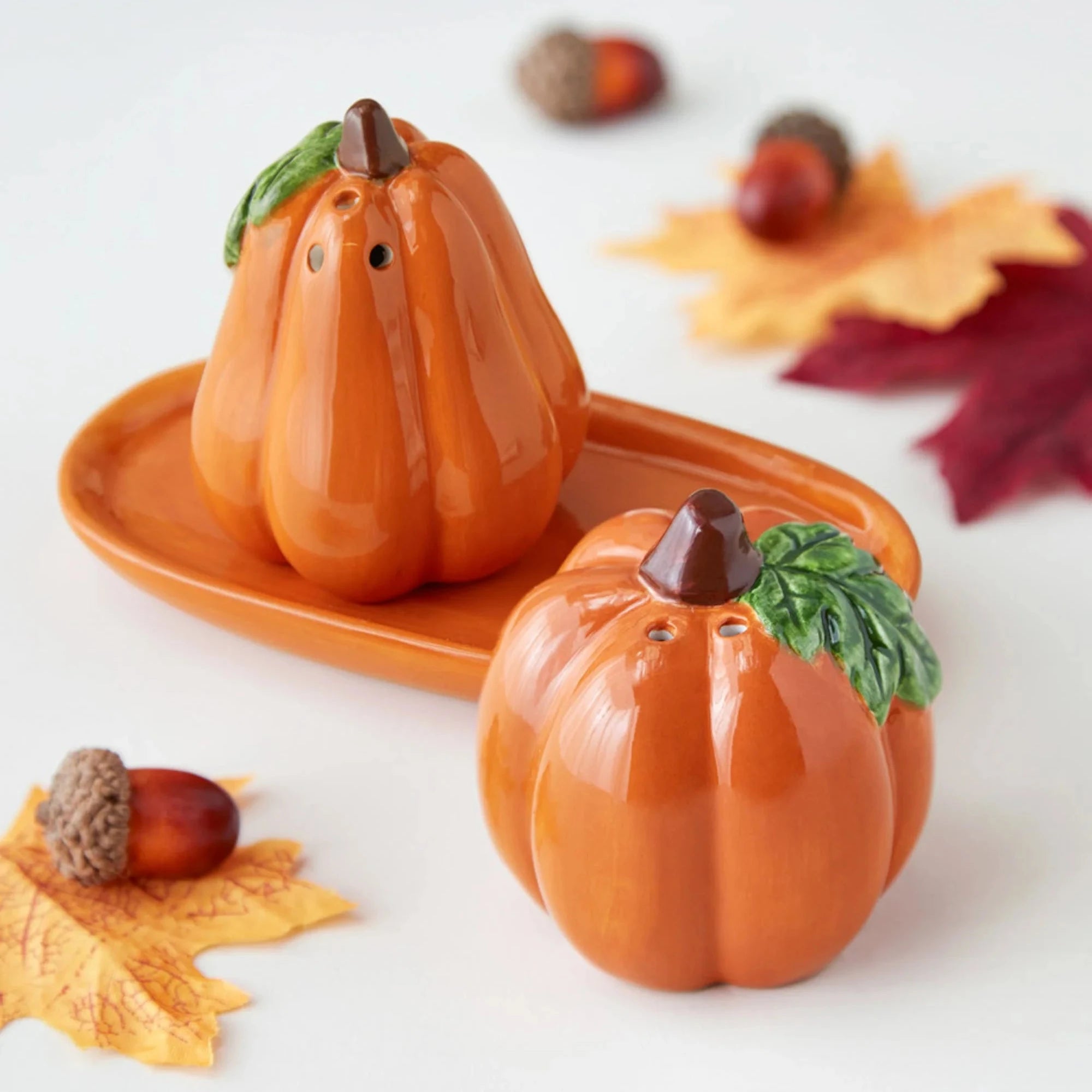 Pumpkin-shaped salt and pepper shakers on a white background with autumn leaves.