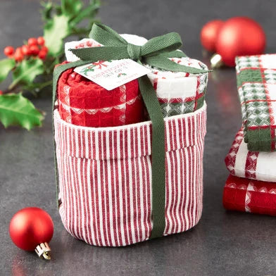 Stacked red and white checkered fabric containers with green ribbons on a dark surface with Christmas decorations.
