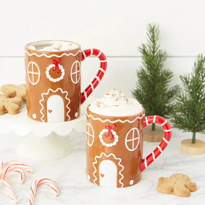 Two gingerbread-themed mugs with candy cane handles on a white surface with Christmas decorations.