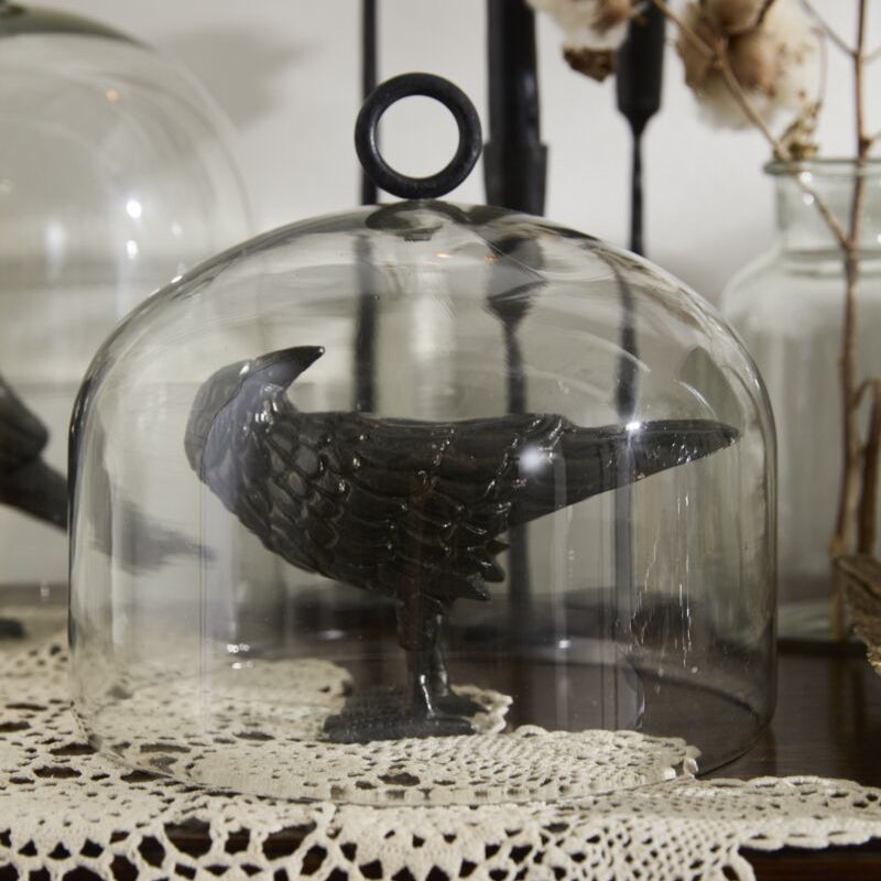 Decorative glass dome with a bird figurine on a lace tablecloth