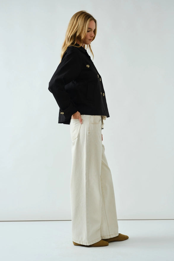 Woman wearing a black jacket and white pants on a white background