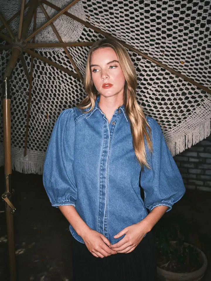 Woman wearing a blue denim shirt standing under a textured white canopy.