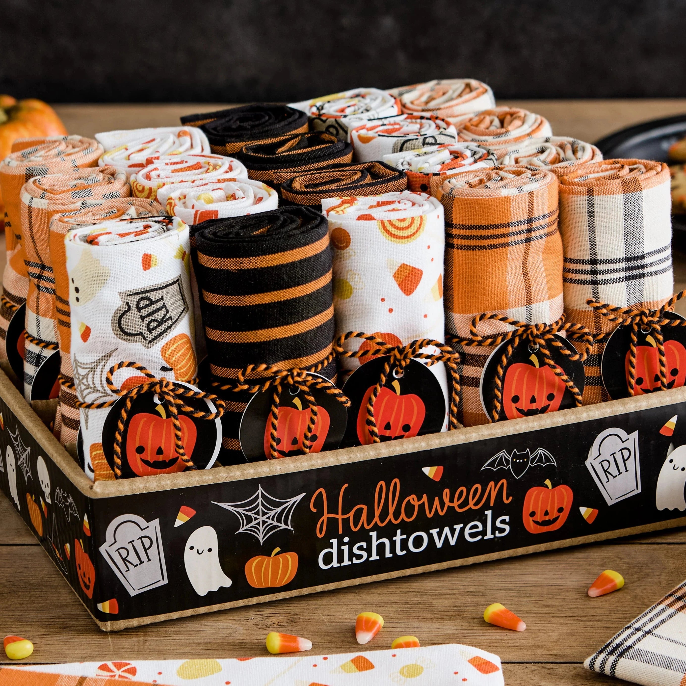 Halloween-themed dish towels displayed on a wooden stand with pumpkins and cookies on a table.