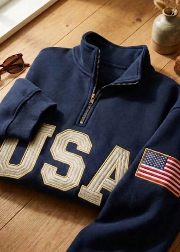 Folded navy blue sweatshirt with 'USA' and American flag on a wooden surface.