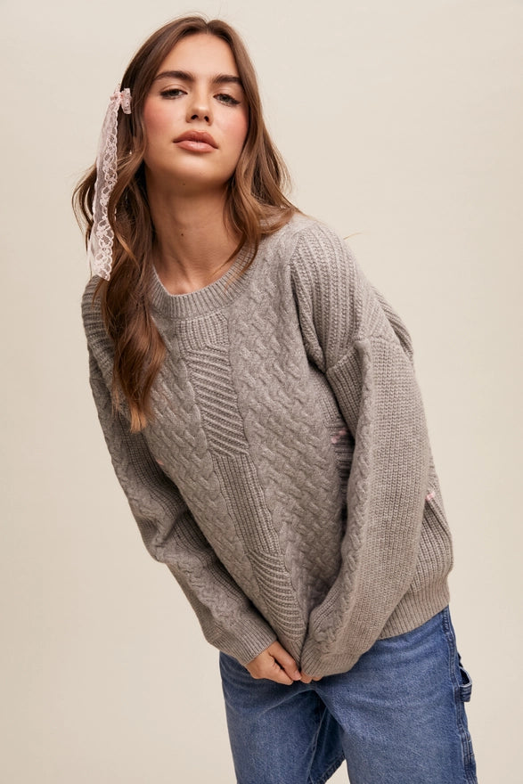 Woman standing against a plain background wearing a heather grey pull over sweater