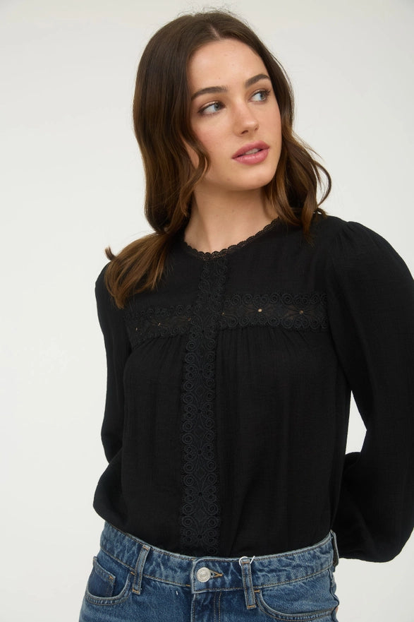 Woman wearing a black blouse with lace details and blue jeans on a white background
