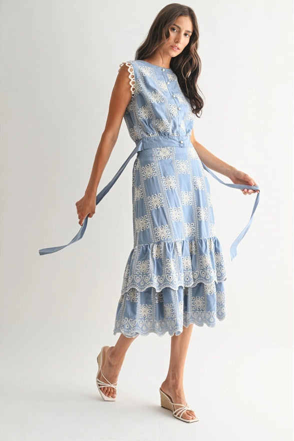 Woman wearing a blue floral dress holding a matching belt against a white background