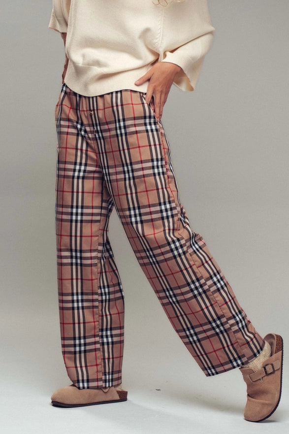 Plaid pants worn with a beige sweater and slippers on a plain background