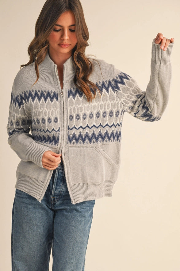 Woman wearing a gray zip-up sweater with blue and white pattern on a beige background