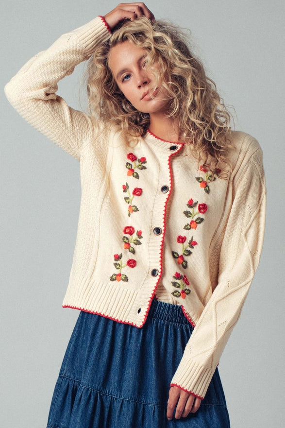 Woman wearing a cream cardigan with floral embroidery on a gray background