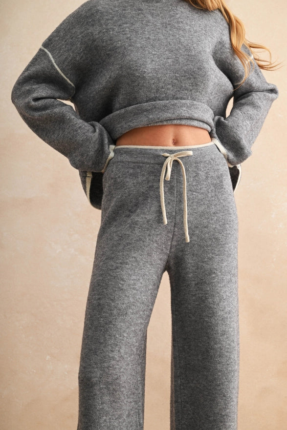 Person wearing a gray sweatshirt and matching sweatpants on a beige background