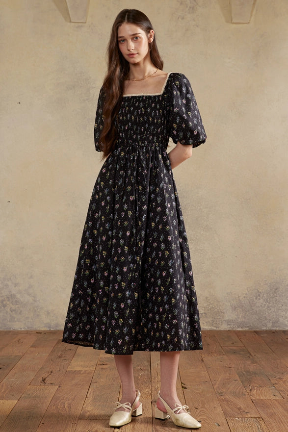 Woman wearing a black floral dress standing against a beige wall.