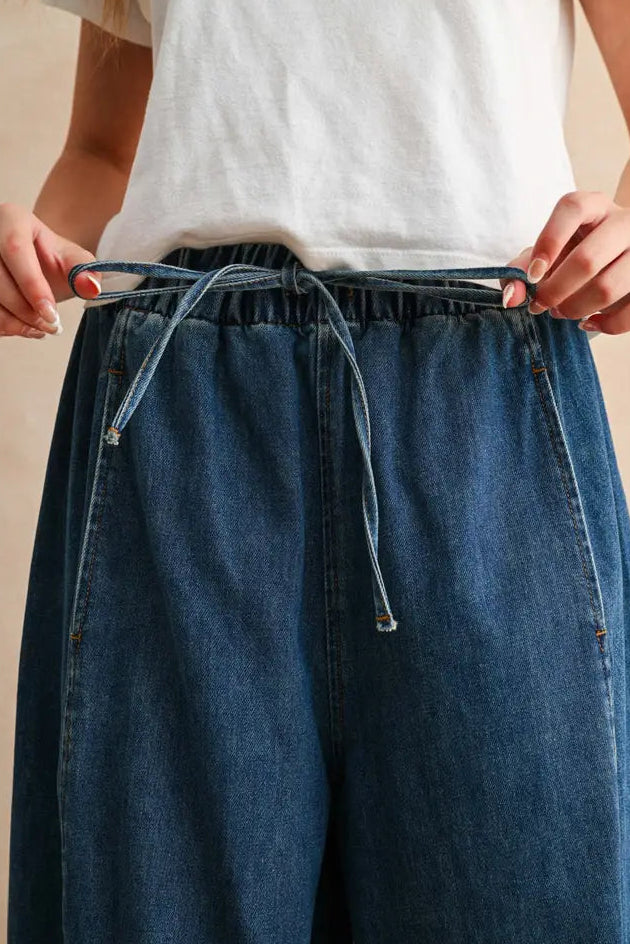 Person wearing blue denim pants with a white top on a neutral background