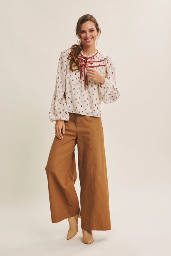 Woman wearing a patterned blouse and wide-leg pants on a plain background