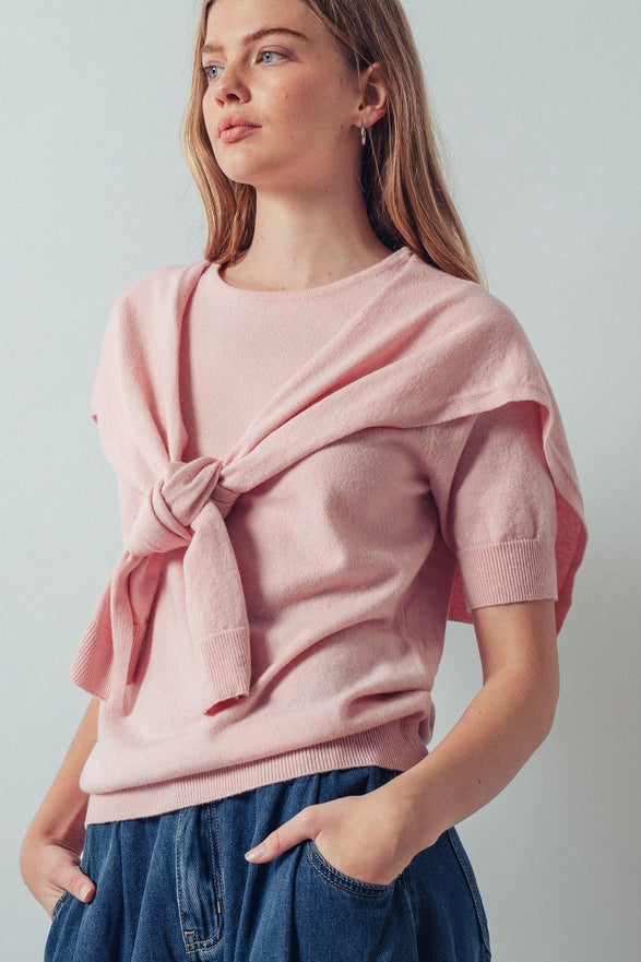 Woman wearing a pink knitted sweater with a knot detail on a plain background