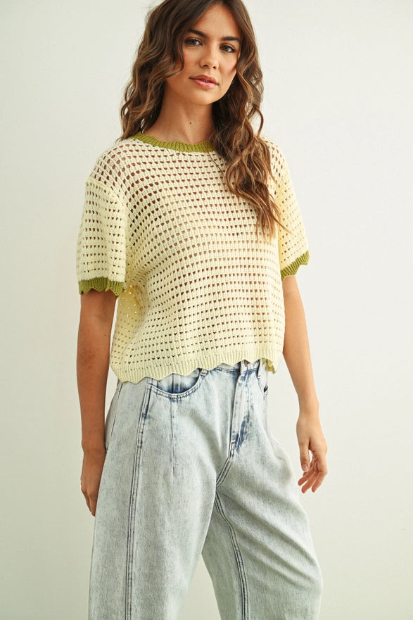 Woman wearing a yellow crochet top and light blue jeans on a plain background