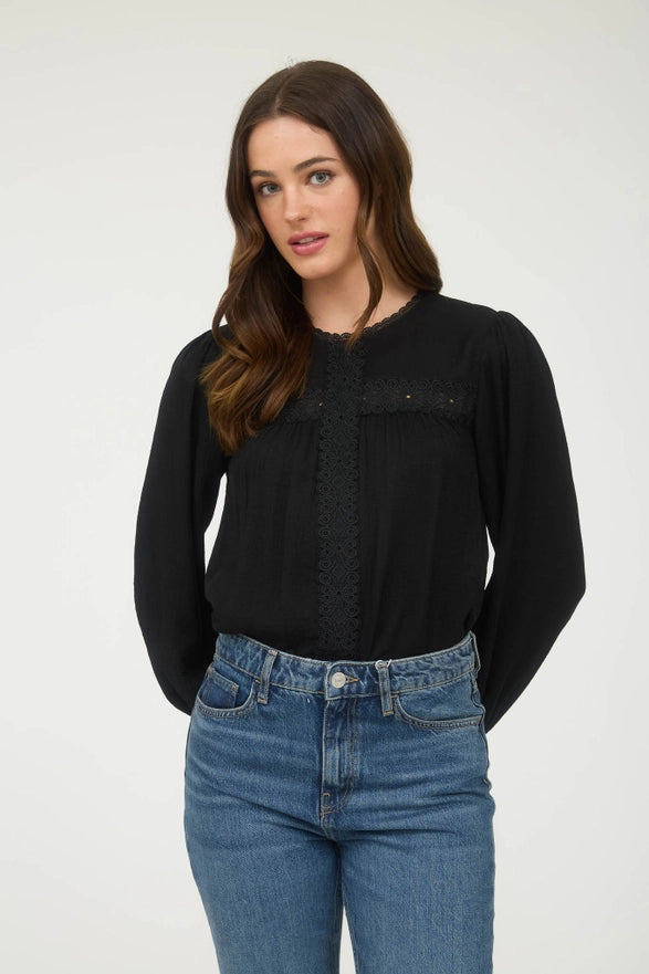 Woman wearing a black long-sleeve top and blue jeans against a white background