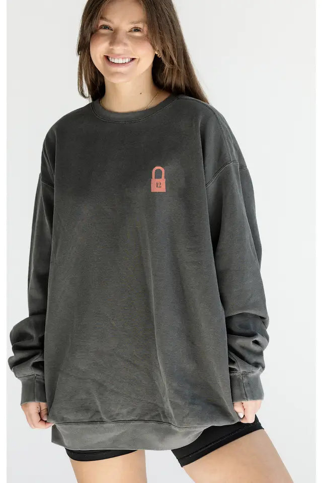 Person wearing a dark gray sweatshirt with a small brown logo on a white background