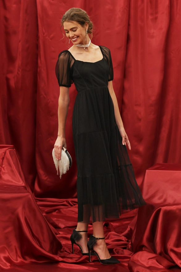 Woman in a black dress standing against a red curtain backdrop