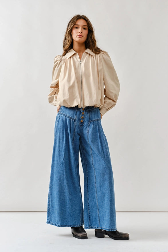Woman wearing a beige blouse and blue jeans against a white background