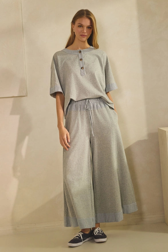 Woman wearing a light gray outfit with wide-leg pants in a neutral setting