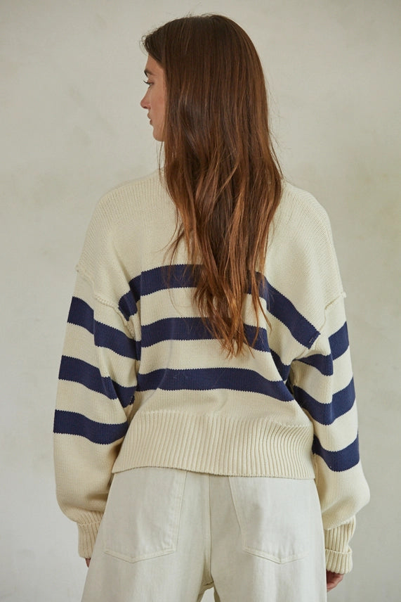 Person wearing a cream sweater with blue stripes from behind on a plain background
