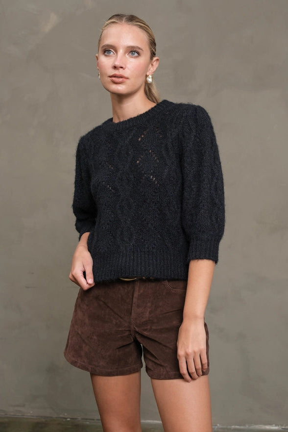 Woman wearing a dark sweater and brown shorts against a plain background