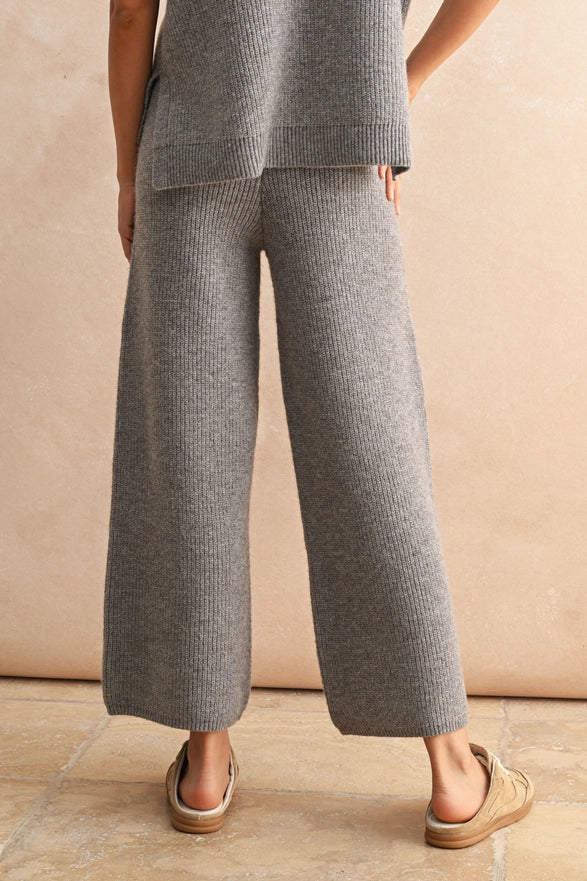 Person wearing a gray knit outfit with wide-leg pants against a beige background