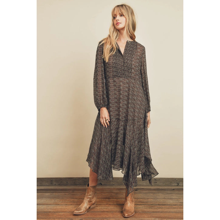 Woman wearing a long, patterned dress with brown boots against a beige wall.