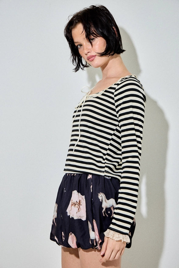 Woman wearing a black and white striped long-sleeve top with a patterned skirt on a plain background