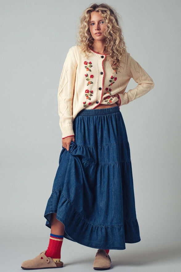 Woman wearing a cream blouse with red buttons and a blue skirt on a gray background