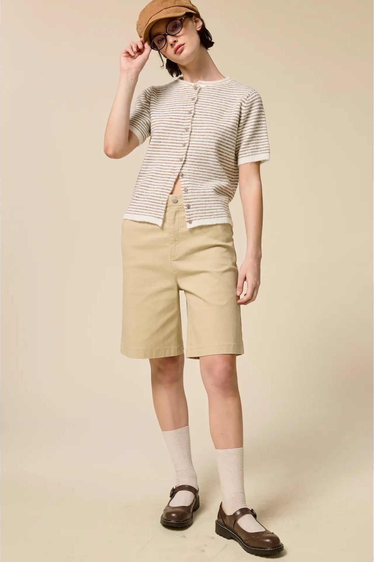 Person wearing a striped shirt, beige shorts, and a hat on a plain background