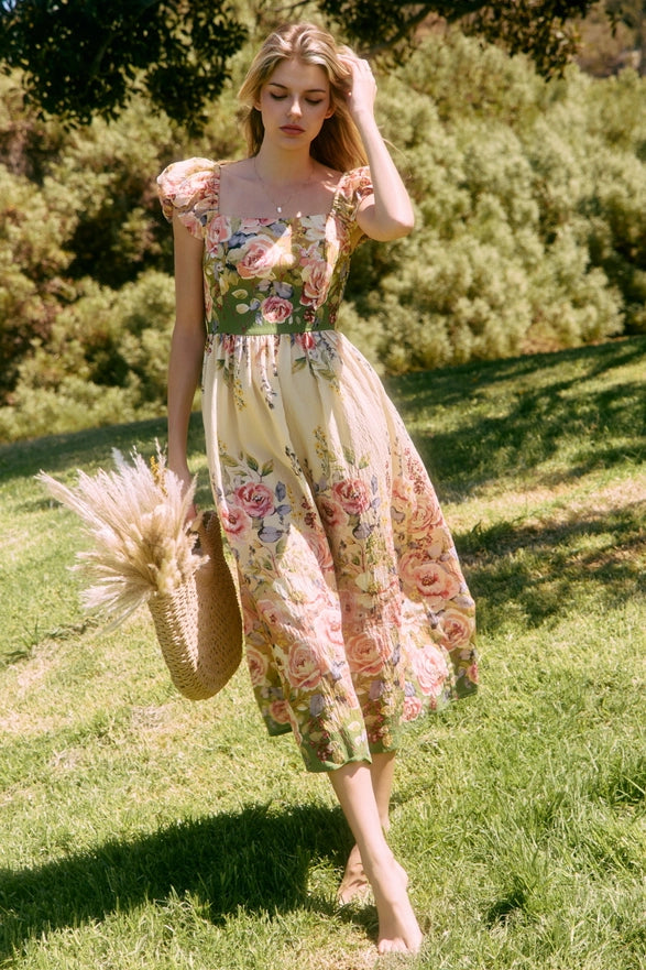 Woman in a floral dress holding a straw bag in a grassy outdoor setting