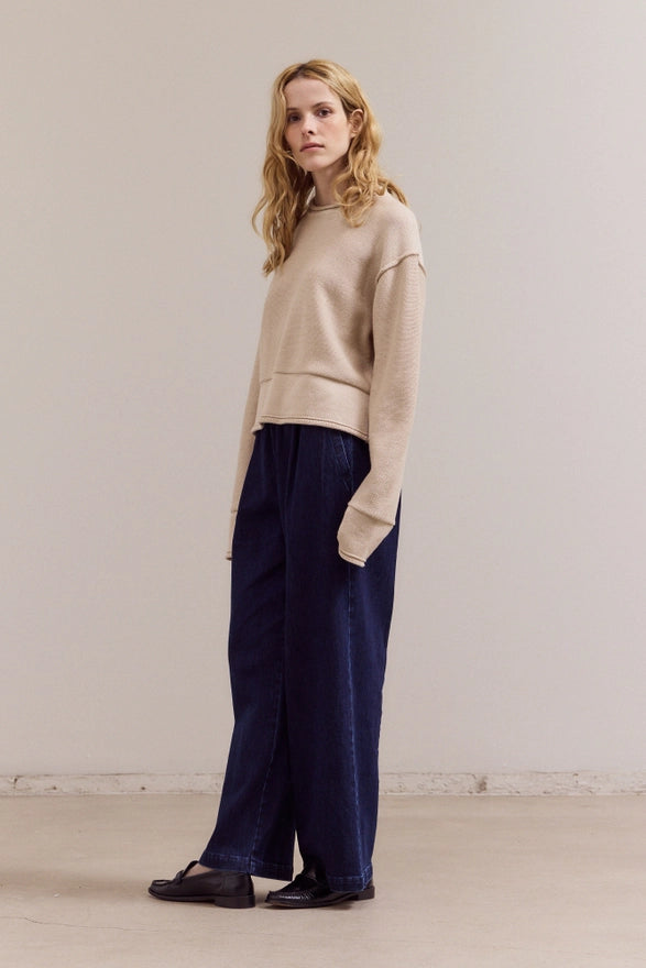 Woman wearing a beige sweater and navy pants against a plain background
