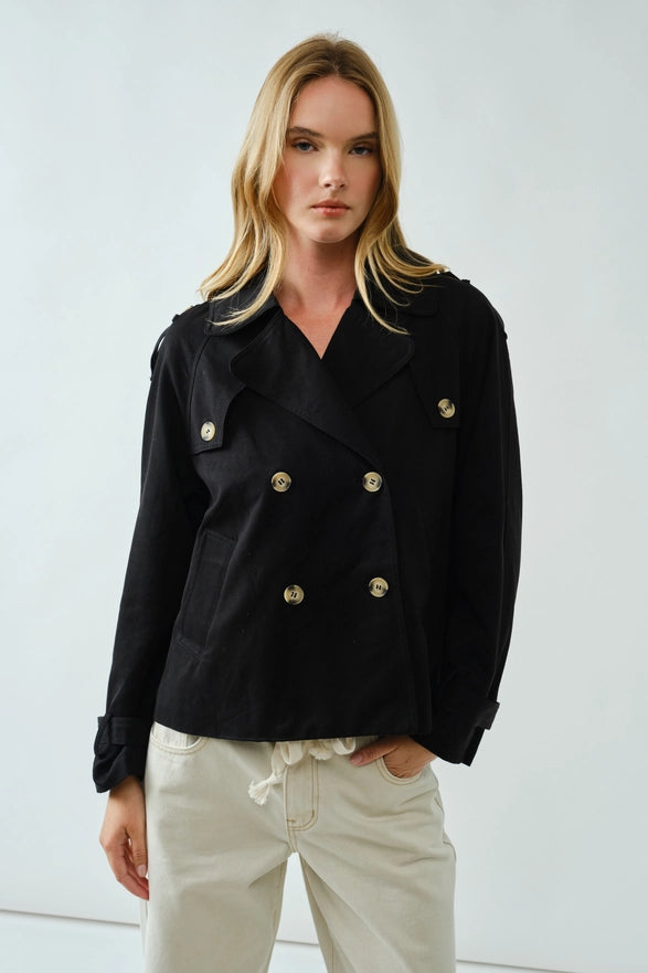 Woman wearing a black coat with gold buttons against a white background