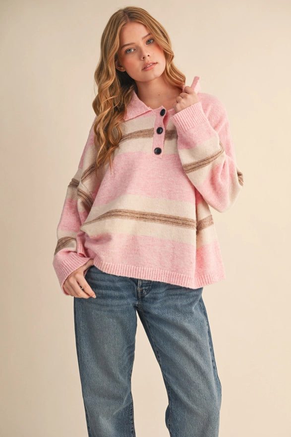 Woman wearing a pink sweater with striped pattern and blue jeans on a beige background