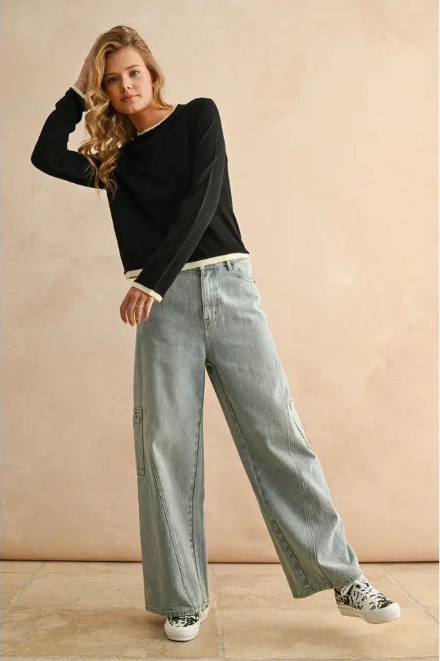 Woman wearing a black sweater and light blue jeans against a beige background