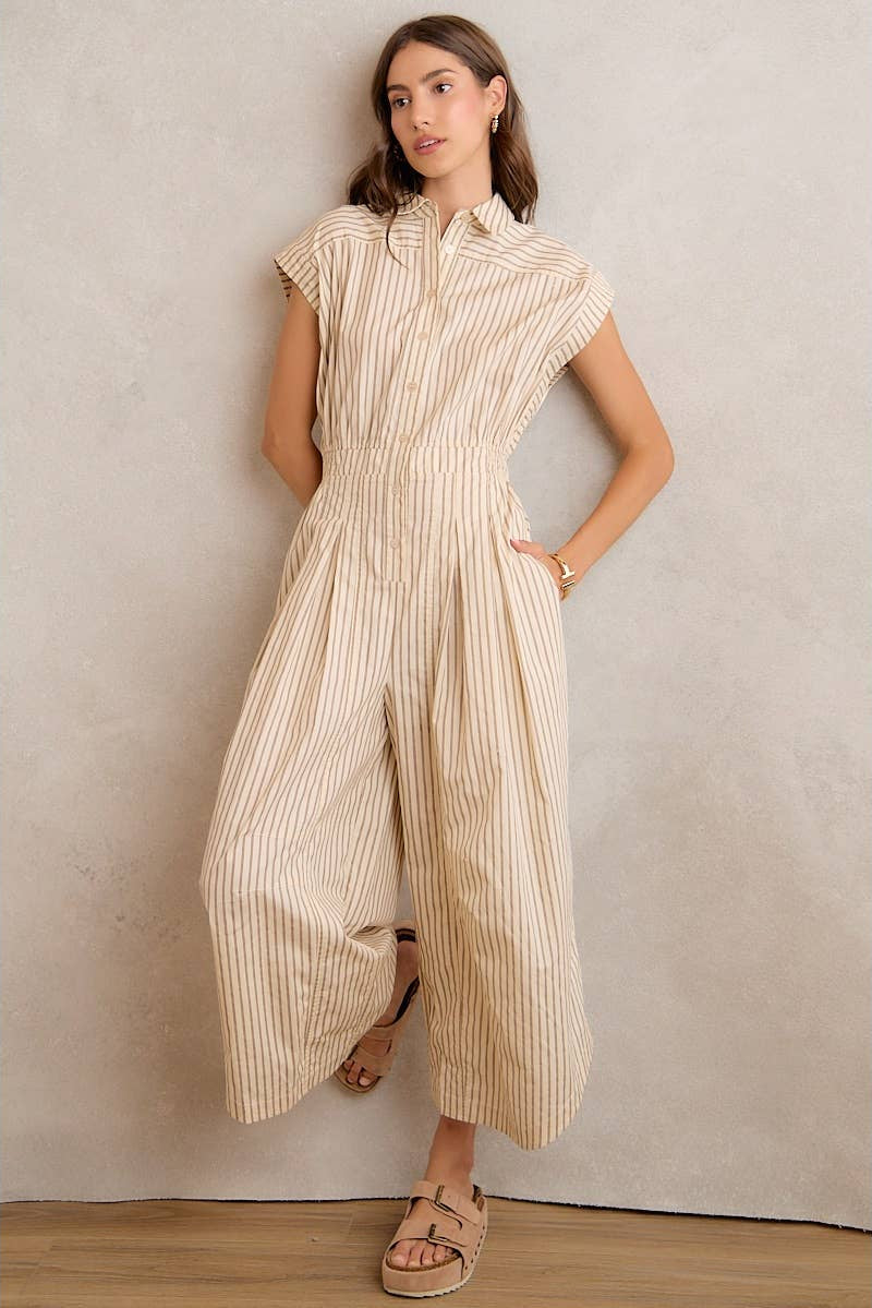 Woman wearing a beige striped jumpsuit against a plain wall.