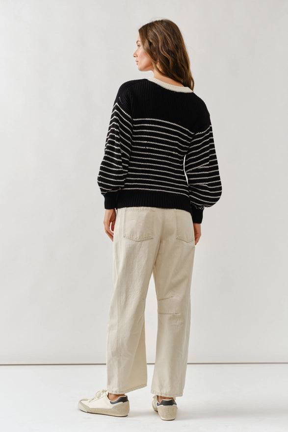 Person wearing a black and white striped sweater and beige pants on a plain background