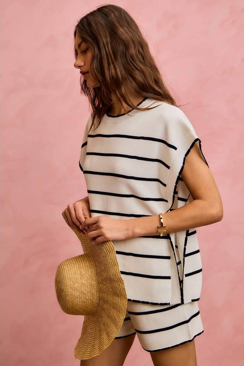 Woman wearing a black and white striped dress holding a straw hat against a pink background