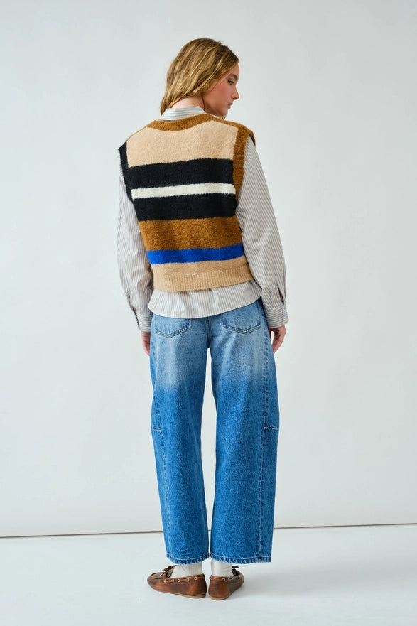 Person wearing a striped sweater vest over a shirt with blue jeans on a white background